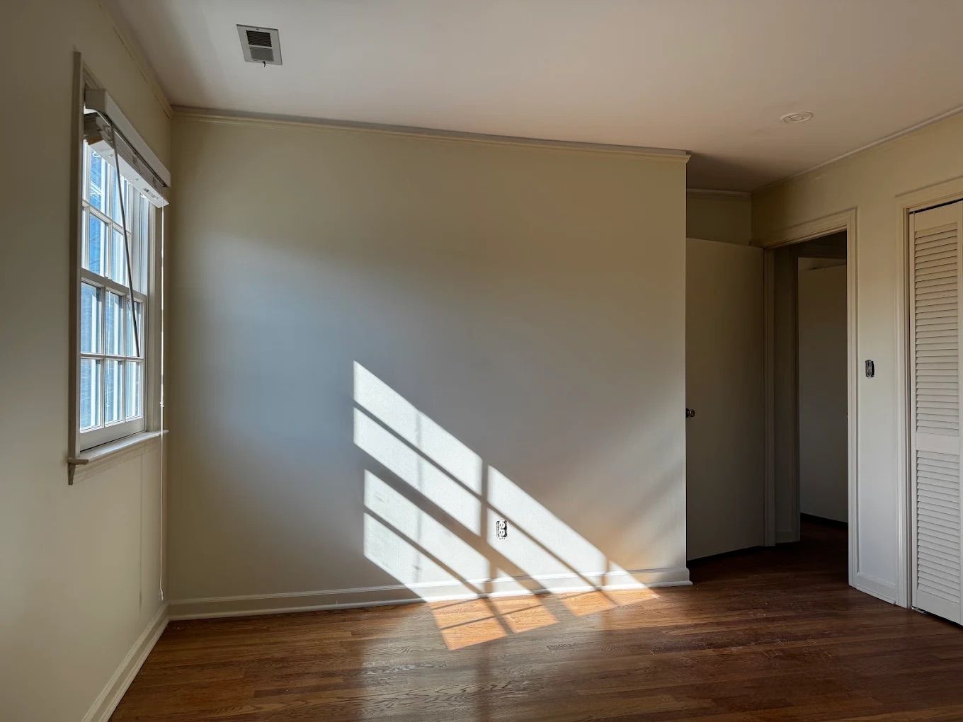 Bedroom freshly painted in soft beige with white window trim and morning sun on the wall