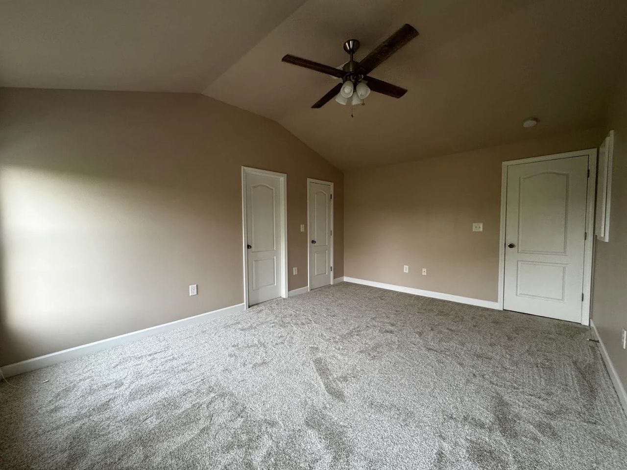 Large primary bedroom with an angled ceiling, beige walls and white doors