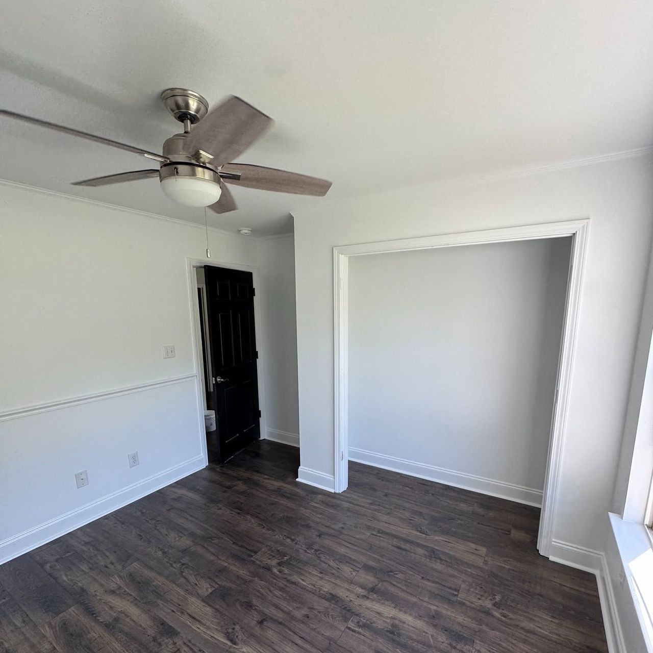 White bedroom with a chair rail, ceiling fan and dark wood floor