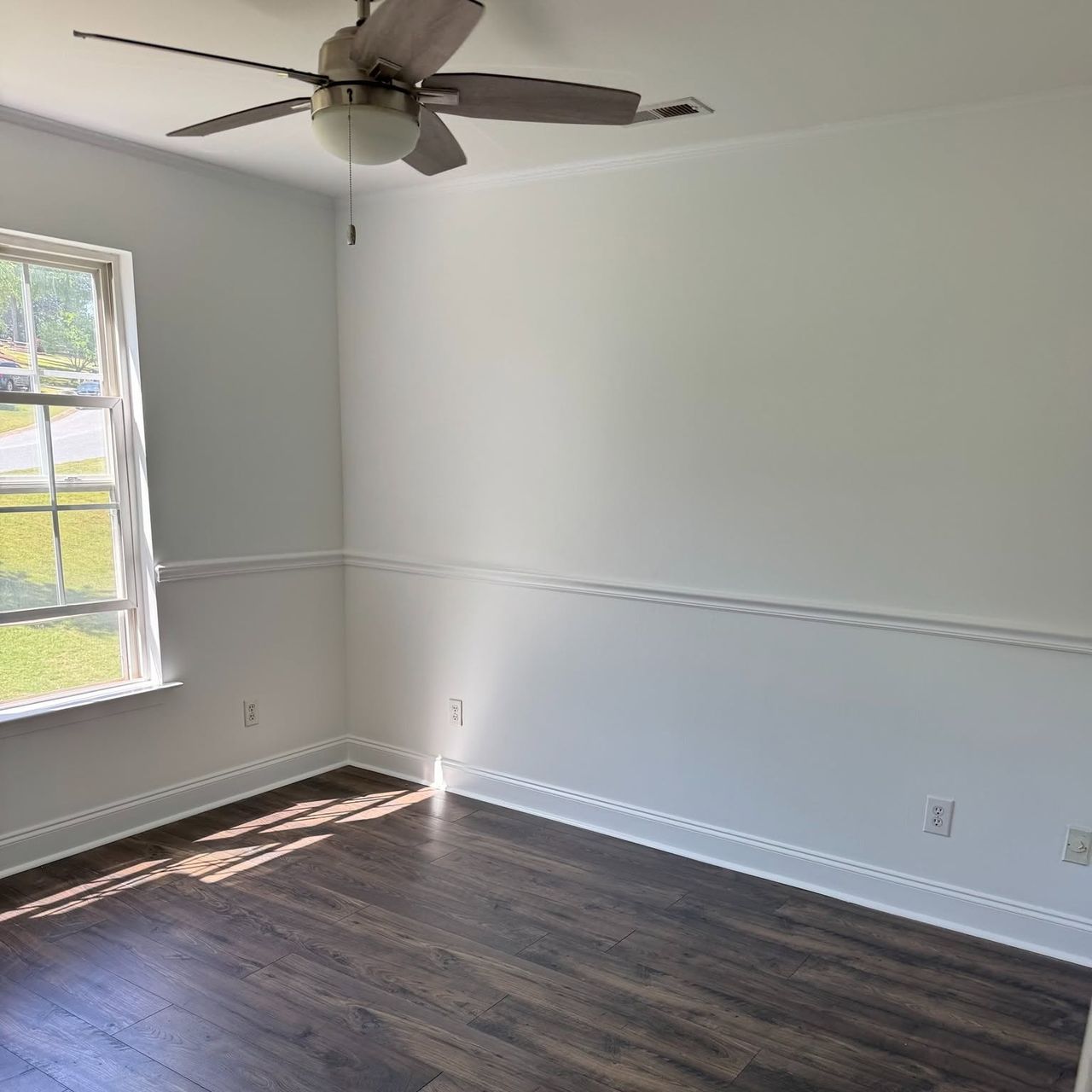 White bedroom with a chair rail, a window and dark wood floor