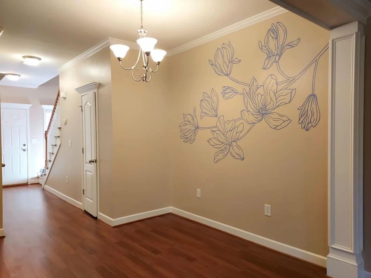 Hand-painted magnolia line drawing in blue-gray on a tan dining room wall with crown molding